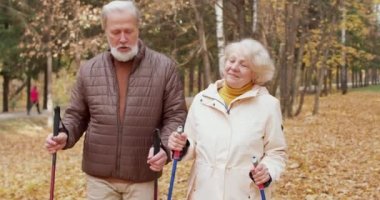 Eski aile İskandinav İskandinav yürüyüşü çubuklarıyla yürüyor. Yavaş çekim, tüm vücudu güçlendirme, fitness rutini, alt vücut dayanıklılığını, koordinasyonu ve dengeyi geliştirme.