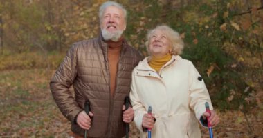 Mutlu çekici yaşlı adam ve kadın sonbahar parkında düşen akçaağaç yapraklarını seyrediyor. Aile altın sezonun güzelliğinden zevk alıyor. Yavaş çekim, çift birlikte huzurlu anın tadını çıkarıyor.