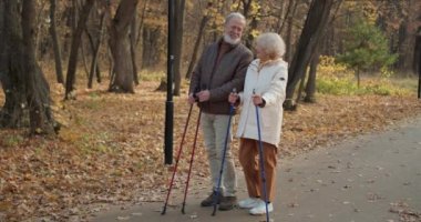 Olgun bir erkek ve kadın, altın sezonda ormanda bastonla yürüyüş yapıyor. Yavaş çekim, yaşlılıkta aktif eğlence kavramı.