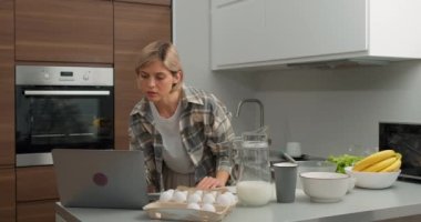 Güzel bir kadın evde tatlı pişiriyor ve yemek tarifi videosu ve özel ders programını dizüstü bilgisayarında izliyor. Masanın üzerinde muz ve un var. Kahvaltı için pasta, krep ya da krema yapma süreci ağır çekim