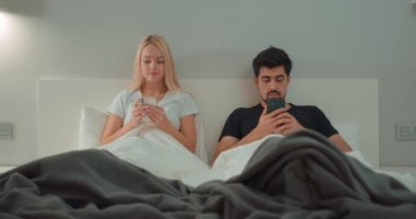 Genç evli bir adam ve kadın gece geç saatlere kadar yatakta oturup akıllı telefonlarıyla oynuyorlar. Sırt sırta verip akıllı telefonlar kullanıyorlar. Evlilik krizi, kayıtsızlık. İlişki Krizi.