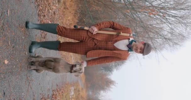 伝統的なイギリスの衣装でハンサムなハンター 犬は森に立っています ハンターは獲物を捜しています ライフスタイルのスローモーション 垂直ショット ペットと優雅な紳士 — ストック動画