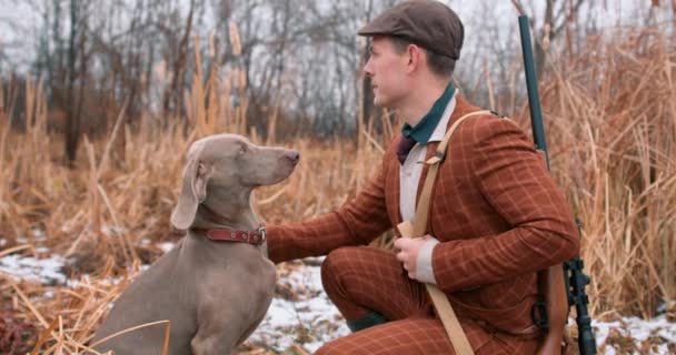スタイリッシュなスーツのエレガントなハンターは 犬と一緒に野生の森で狩猟中の彼のワイマランナーの犬をストロークします スローモーションガイ 探しているいくつかのゲーム 男性は 横向き 狩りに準備 — ストック動画