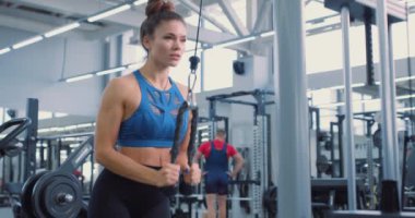 Spor salonundaki hareketli kadın spor aletlerini yavaş çekimde çekiyor, yaşam tarzı, hobi, ilgi alanları, trisepsleri aşağı itiyor. Silah egzersizleri. Motivasyon, meydan okuma