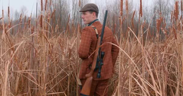 Şapkalı Yakışıklı Bir Avcı Sırtında Bir Silah Sonbahar Tarlasına Bakıyor — Stok video