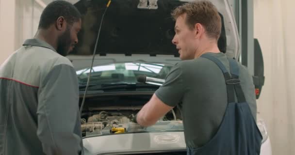 Zwei Männliche Mechaniker Unterhalten Sich Der Garage Vor Dem Auto — Stockvideo