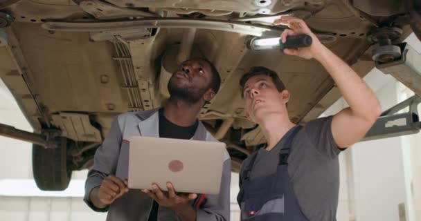 Dos Mecánicos Afroamericanos Caucásicos Hombres Pie Bajo Coche Roto Garaje — Vídeo de stock