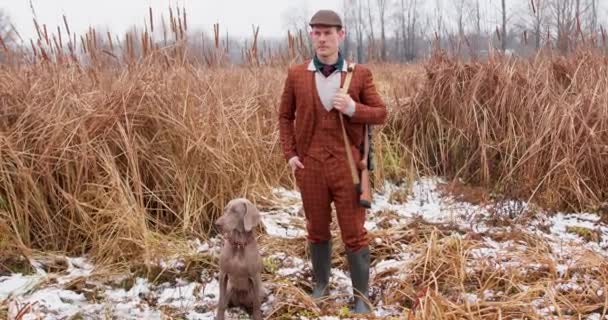 スーツ ブーツを着たハンター男は 池の遅い動きアドベンチャー 狩猟のファッションで彼の犬と離れて立っている — ストック動画