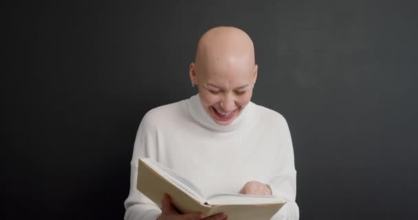 年轻有趣的秃头女人拿着书 在孤独的黑色背景下开心慢动作快乐兴奋的女孩阅读有趣的童话故事休闲小说迷知识教育 — 图库视频影像