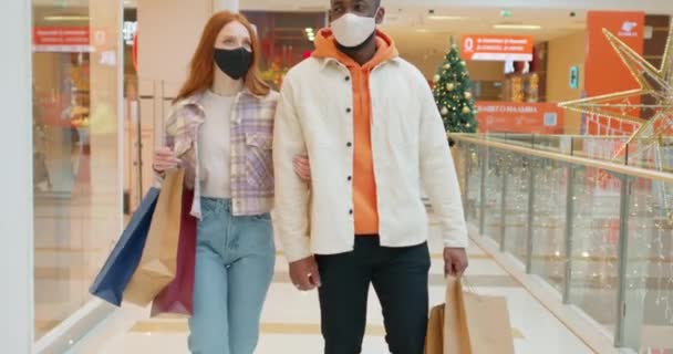 若い混合レース 百貨店の屋内多様な家族のショッピング 魅力的なカップルは フェイスマスクを着用し 幸せと一緒にショッピングバッグを保持し ショッピングモールセンターで購入を楽しむ — ストック動画