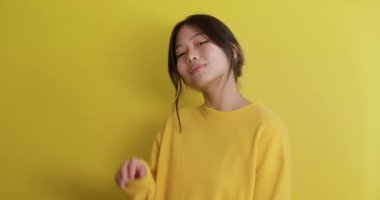 Utangaç genç kız flört ediyor, merhaba diyor, üflüyor, gülüyor, elleriyle ağzını kapatıyor, avuç içi sarı arka planda. Yavaş çekim Flirt, Aşk, Kadın tatlı öpücükler yolluyor..