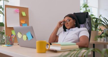 Yorgun ve yorgun genç siyahi kadın öğrenci, online işlerde kısa bir ara veriyor. Koltuk başında uzanan aşırı çalışan kadın, yorgunluk hissediyor. Yavaş çekim, depresyon.
