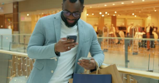 快乐的非洲裔美国人 很多购物袋都是用智能手机在线购物 手里拿着信用卡慢动作销售黑色星期五很容易支付礼品卡销售提供电子商务人享受季节销售 — 图库视频影像