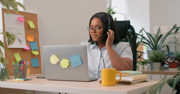一位戴着耳机的黑人快乐女性客户服务操作员坐在办公室里通过视频通话 呼叫中心代理通过使用笔记本电脑回答投诉和问题 向客户提供建议 — 图库视频影像