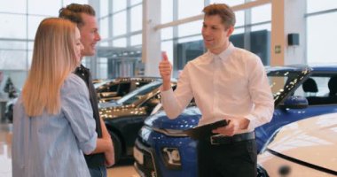 Dost canlısı araç satıcısı genç aileye yeni bir araba gösteriyor, ağır çekimde. Genç bir çift galeride yeni bir araba seçiyor ve galeri temsilcisine danışıyor. İkinci el arabalar satılık.