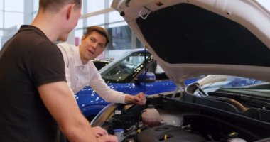 Adam yeni bir araç alıyor açık kaputlu bir otomobilin motorunu kontrol ediyor profesyonel bir telif alanı motorlu araba sürücüsüyle konuşuyor kira kontratı öneriyor. Yavaş çekim