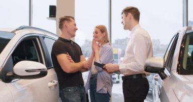 Kadın, kocasına modern bayilik merkezinde araba alması için yalvarıyor. Adam da kabul ediyor, mutlu kız arkadaşına sarılıyor. Yavaş çekim, doğum gününde hediye. mutluluk