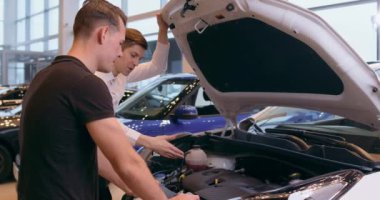 Genç pazarlamacı yeni bir araba gösteriyor, müşteri için motor, arabanın kaputunu açan adam ağır çekim, arabada oturan ve el sallayan mutlu kadın..