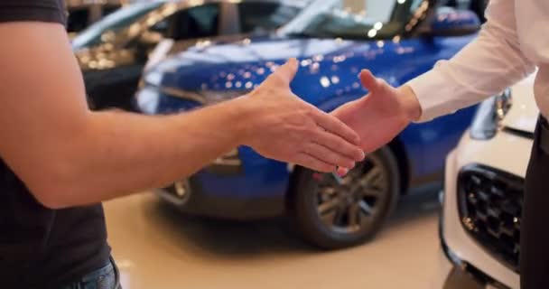 買った車のバックグラウンドで車のディーラーで握手する2人の男性顧客とクライアント 成功した購入 自動車ディーラーのショールームでの取引 スローモーション クローズアップされたショット — ストック動画