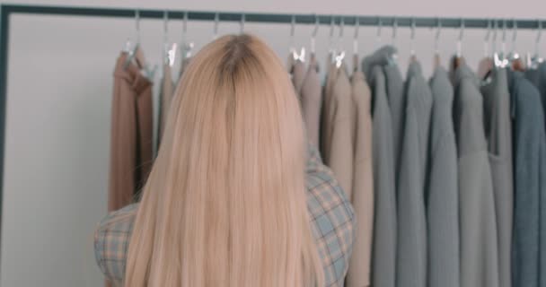 ブロンド女性の顧客は ショッピングモールで服を選択します バックレアビューショップアシスタント販売 ファッショナブルな衣服のスローモーション販売を選択 — ストック動画