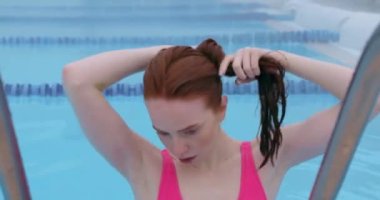 Moda pembesi mayo giyen güzel bir kız, ıslak saçlarıyla sudan çıkar, hayattan zevk alır, kollarını kaldırmış, saçlarını topuz yapar, yüzme havuzunda ayakta duran bir kadın saçlarını toplar.