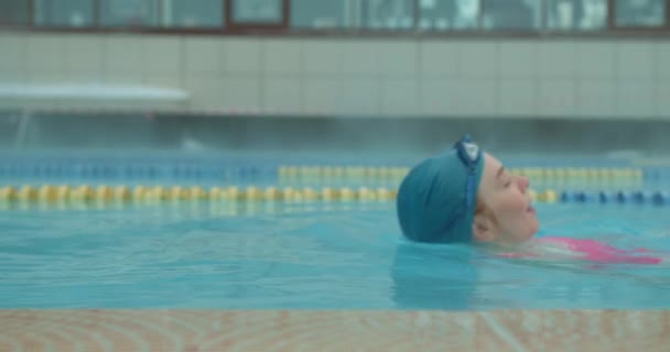 屋外のサーマルプールで泳ぐブルーキャップのリラックスした女性 スローモーションソフトフォーカスサイドビューショットスポーツヘルスウェルネス ウォータースプラッシュ — ストック動画
