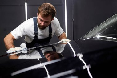 Adam arabayı temizliyor ve mikrofiber bezle aracı kurutuyor. Erkek, cilalama ve seramik kaplamadan sonra parlak siyah arabanın boya yüzeyini temizler. Araba yıkama ve araba yıkama konsepti