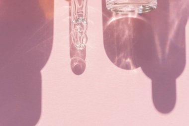 Güzellik projen için pembe arka planda yüz serumu ve şişe gölgesi olan pipo damlası.