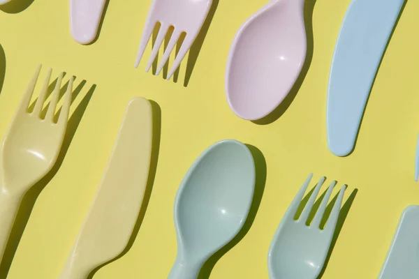 stock image close up pattern of multi-use plastic cutlery on a pastel yellow background