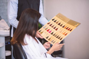 Kuaför, güzel bir kadına tavsiyelerde bulunuyor. Kuaför, kuaför salonundaki yeni saç rengini seçiyor..