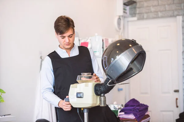 サロンで顧客にサービスを提供するためにヘアスチーマーを準備プロの美容師の男 — ストック写真