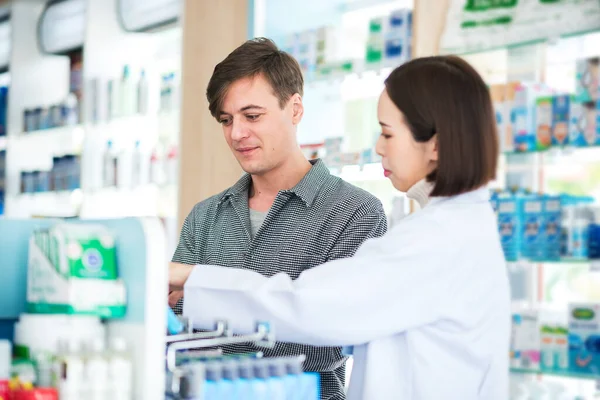 Asian pharmacist advising patient caucasian customer about healthcare product and medicine instructions in pharmacy.