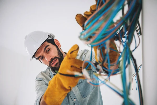 Portrait of caucasian man electrical engineering construction worker wearing hardhat and safety equipment, checking electrical system at construction site.