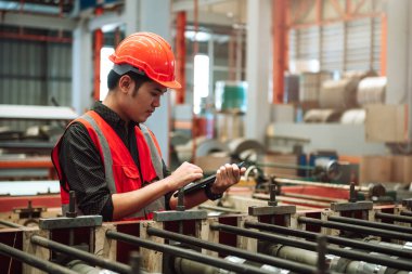 Fabrikadaki makine sistemini denetlemek için tablet kullanan koruyucu kask takan fabrika işçisi mühendisi. Heavy metal endüstrisi üretim fabrikası.