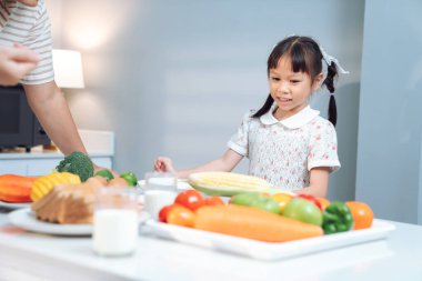 Neşeli genç bir kız hamile annesine mutfakta yardım ediyor, sağlıklı beslenme ve takım çalışmasını desteklerken besleyici bir yemek hazırlıyor, aile bağlarını ve evde bakımı ön plana çıkarıyor.