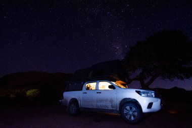 Milky way over a tent located on the roof of a pickup car in the Namib desert of Namibia.