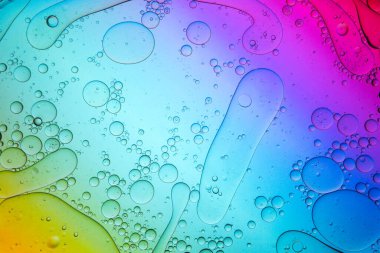 Yukarıdan çeşitli şekillerde kaotik su damlaları şeffaf yüzeyde karışıyor renkli ışıklarla aydınlatılıyor.