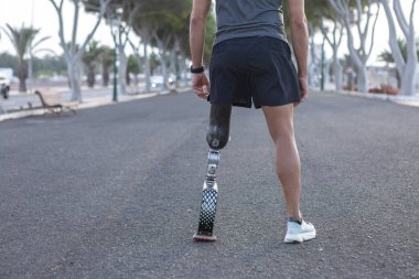 Arka planda, spor kıyafetleri içinde kimliği belirsiz bir erkek ampütasyon şehir parkında koşuya hazırlanırken görülüyor.