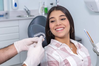 Diş kliniğinde danışmanlık yaparken diş hizalayıcılarını İspanyol ergen kızlara nasıl kullanacağını açıklayan eldivenli anonim erkek stomatolog.