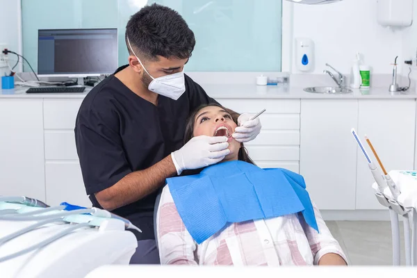 ヒスパニック男性歯科医で制服で手袋と顔マスク検査歯の十代の若者の仕事中に現代歯科クリニックで昼間 ストックフォト