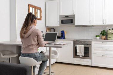 Evinde dizüstü bilgisayar kullanarak sırt üstü oturan tanınmayan bir kadın.  