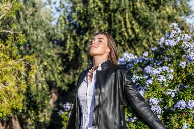 20 yaşında, gözleri kapalı, şehir parkının temiz havasını soluyan beyaz bir kadın..