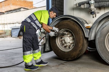 Üniformalı ve eldivenli erkek makine mühendisi gündüz vakti garajda çalışırken kamyonu eğip sıkıyor.