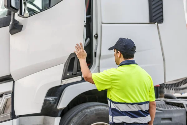 Back view of anonymous concentrated male driver in casual t shirt and cap standing near truck while opening door to commence driving in daylight