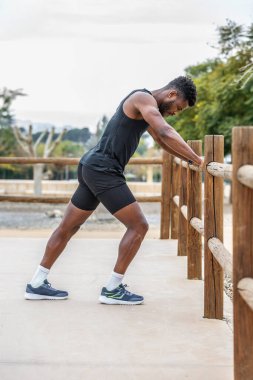 Aktif giyinmiş genç Afrikalı Amerikalı erkek sporcunun vücut tarafı antrenmandan önce ısınırken bacaklarını esnetiyor.