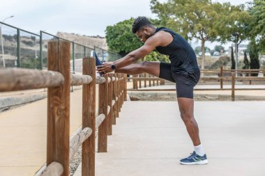Güçlü Afrika kökenli Amerikalı sporcunun tahta çitin üzerine bacağını koyması ve spor yaparken ayak parmağı egzersizi yapması.