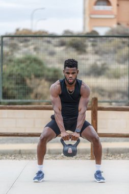 Afrika kökenli Afrikalı Amerikalı erkek sporcu ağır kettlebell kaldırıyor ve fonksiyonel eğitim sırasında derin nefes alıyor.