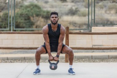 Ağırlık kaldırma eğitimi sırasında ağır kettlebell ile çömelme hareketleri yapan kararlı Afrikalı Amerikalı erkek sporcu.