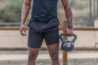 Anonim Afrikalı sporcu, spor kaslı, dar siyah spor giyimli, ağırlık kaldırma antrenmanı sırasında elinde ağır bir kettlebell tutan.