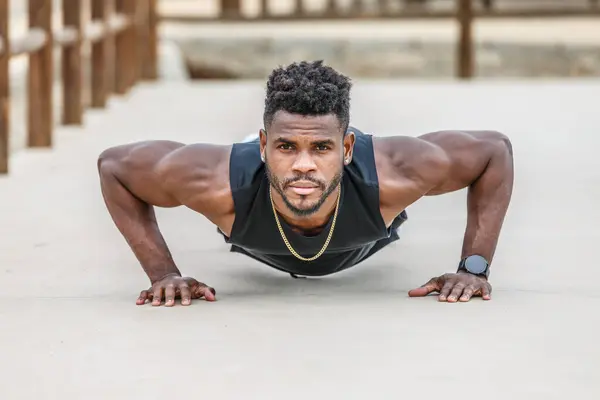 Strong African American male athlete in sportswear with Afro hair doing push ups on ground during functional training
